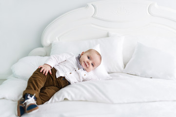 The charming and quiet kid in clothes lies on white blanket in bedroom