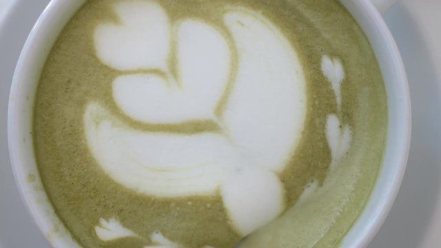 Close-up shot of barista creating cream picture of abstract flower on latte matcha, making drops
