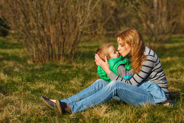 Mom and her son are sitting and hugging on the lawn.