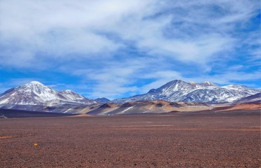 Long shot of the landscape surrounding Laguna Verde with snow captured mountains, brown hills and volcanic stones and rocks in Chile, South America