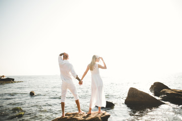 Romantic loving couple posing on stones near sea, blue sky