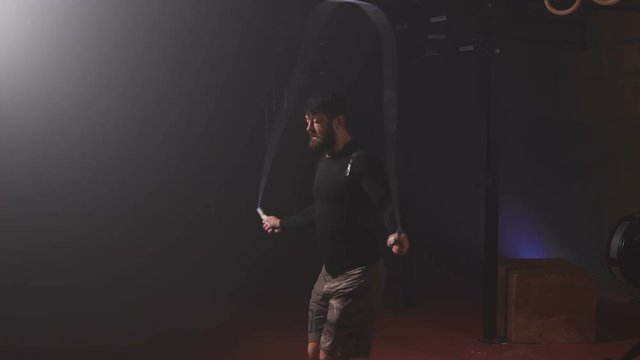 Strong sportsman with beard in black t-shirt doing jumping rope exercise.