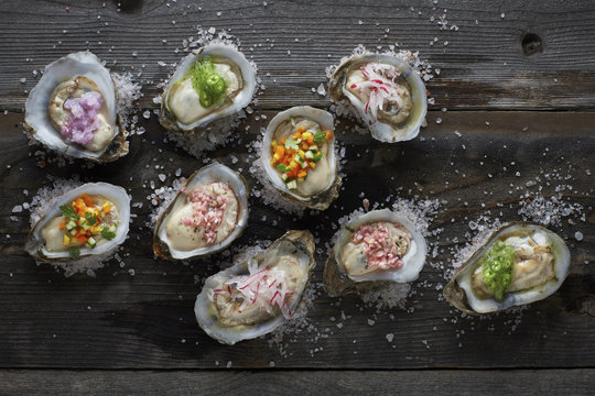 raw oysters on the half shell topped with an assortment of different colorful sauces, sitting on a rustic wood table