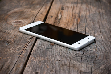Smartphone mit randlosem Display auf rustikalem Holzuntergrund, Vignettierung