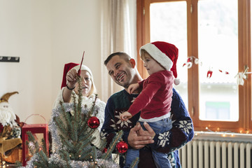happy family with a young child decorating a christmas tree at h