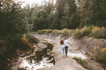 Fototapeta premium Young couple running near the river and rocky shore