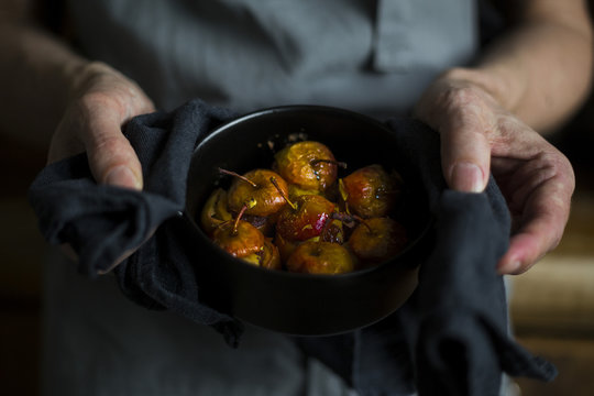 Close-up of man's hands holding cocotte with stuffed roast apple