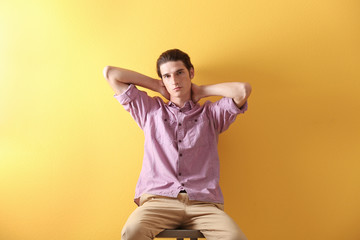 Fototapeta na wymiar Handsome young man sitting on stool on yellow background