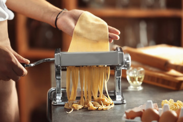 Man using pasta machine to prepare tagliatelle, close up view