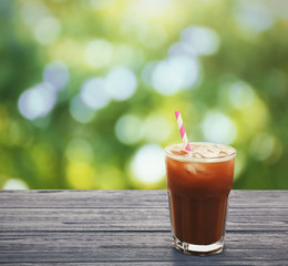 Glass of cold coffee on wooden table against blurred nature background