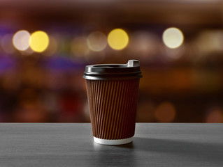 Paper cup of coffee on wooden table against blurred background.