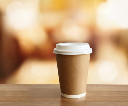 Paper cup of coffee on wooden table against blurred background.