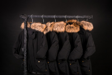 lot of black coats, jacket with fur on hood hanging  clothes rack.  background. © bondarillia
