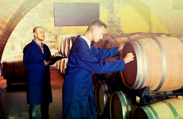 two men in uniforms taking notes in cellar with wine woods