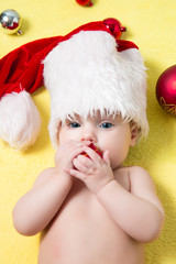 Baby in a red Santa hat with balls on the New year tree. Beautiful little  celebrates Christmas