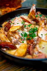 Oven baked potatoes with cream and cheese in black  in a frying pan on wooden table. Close up. Tasty food.