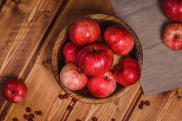 Red apples in a bowl on a wooden table, with beige cloth and star anise. Top view.