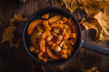 Top view of old pan with fried pumpkin with garlic on a vintage table with autumn leaves and star anise