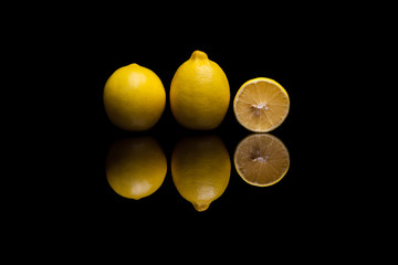 Two isolated yellow lemons and one halved on black background