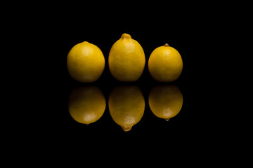 Three whole isolated yellow lemons on black background