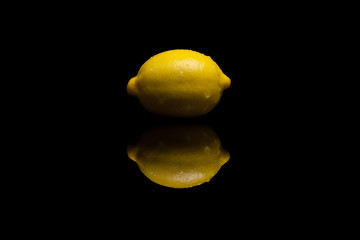 One whole isolated yellow lemon on black background
