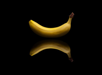 Single yellow banana on black reflective background