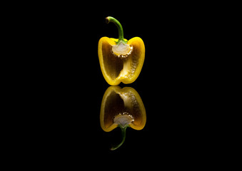 One halved yellow pepper on black reflective background
