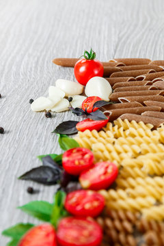 Mixed of two colored pasta near tomatoes, garlic and basil on grey wooden  background. Close up  raw .