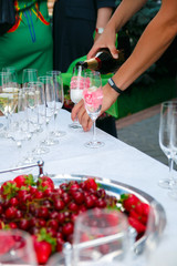 Reception table. Pour in wineglass. Glasses of wine, champagne, plates and berries on the white tablecloth. Catering business.