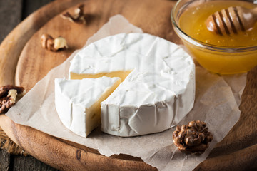 Brie type of cheese. Camembert cheese. Fresh Brie cheese and a slice on a wooden board with nuts, honey and leaves. Italian, French cheese.