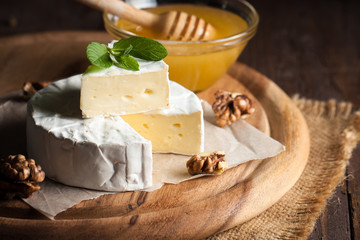 Brie type of cheese. Camembert cheese. Fresh Brie cheese and a slice on a wooden board with nuts,...