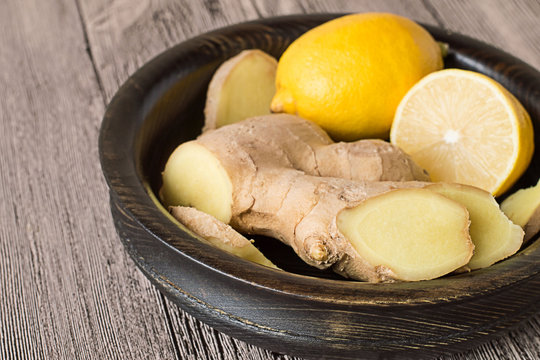   Lemon and ginger root.  Lemon and ginger root in a wooden bowl on a gray wooden table.