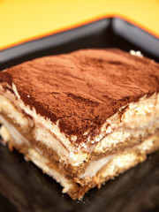 Tiramisu cake in a black plate, close up, vertical shot
