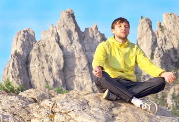 Naklejka na ściany i meble Man Traveler Relaxing Yoga Meditation sitting on stones with Rocky Mountains peak Ai-Petri and blue sky on Background