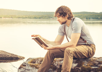 Fototapeta premium Young Man reading book outdoor with lake on background Summer va