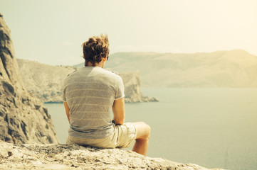 Young Man relaxing on rocky cliff  Sea and mountains on background Lifestyle Summer vacations concept retro colors