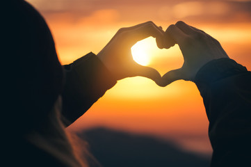 Woman hands Heart symbol shaped silhouette Travel Lifestyle and Feelings concept with sunset sky nature on background