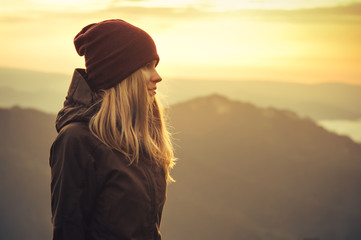 Young Woman standing alone outdoor with sunset mountains on background Travel Lifestyle and survival concept rear view - obrazy, fototapety, plakaty
