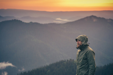 Young Man bearded standing alone outdoor with sunset mountains on background Travel Lifestyle and survival concept - obrazy, fototapety, plakaty