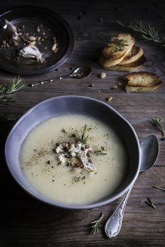 Cauliflower cream soup in bowl with grilled bread slices on wood