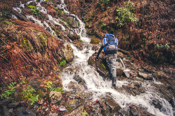 Man Traveler with backpack crossing waterfall in mountains Travel Lifestyle concept  Summer vacations activity outdoor extreme sport