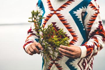 Man hands holding fir tree branch Fashion Travel Lifestyle wearing knitted sweater outdoor foggy nature on background