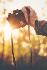 Fototapeta na wymiar Hand holding retro photo camera shooting sunset outdoor Travel Lifestyle with autumn nature on background
