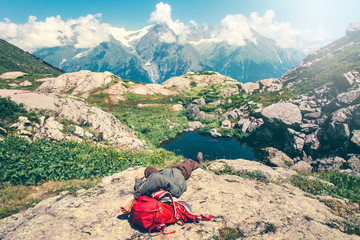Fototapeta premium Man laying relaxing with backpack on rocks Travel Lifestyle concept serene view of mountains landscape summer vacations outdoor
