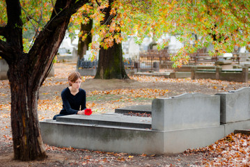 Young Woman Dressed in Black Laying Flower on Grave in Cemetery in Fall