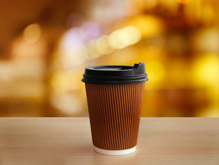 Paper cup of coffee on wooden table against blurred background.