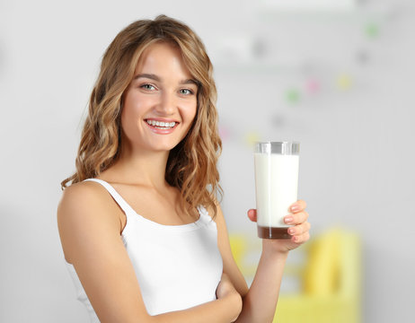 Young woman with glass of milk on blurred interior background.