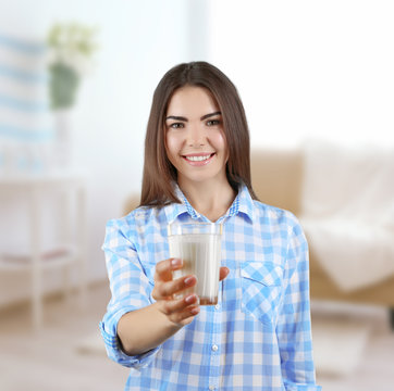 Young woman with glass of milk on blurred interior background.