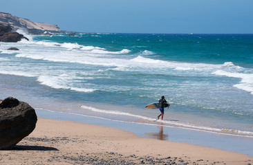 Fuerteventura, Isole Canarie: un surfista sulla spiaggia nera di Playa de Garcey, la spiaggia dove...