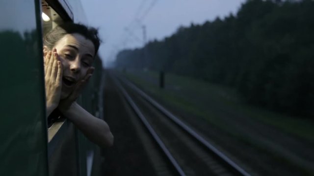 Night portrait of happy female girl smiling and screaming throw the opened train window in train
